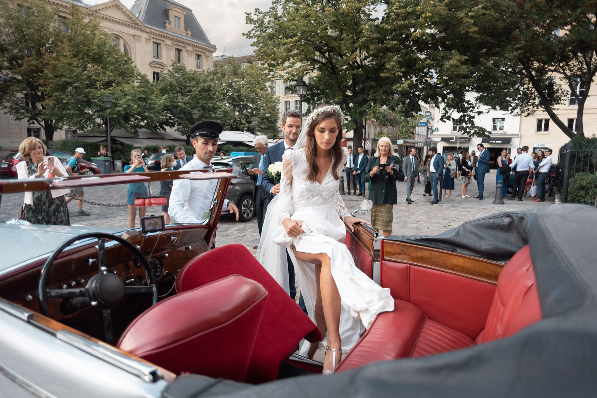 La mariée monte dans la voiture de collection qui l'attend à la sortie de la cérémonie religieuse à Saint Germain des Prés à Paris, par Etienne Ster